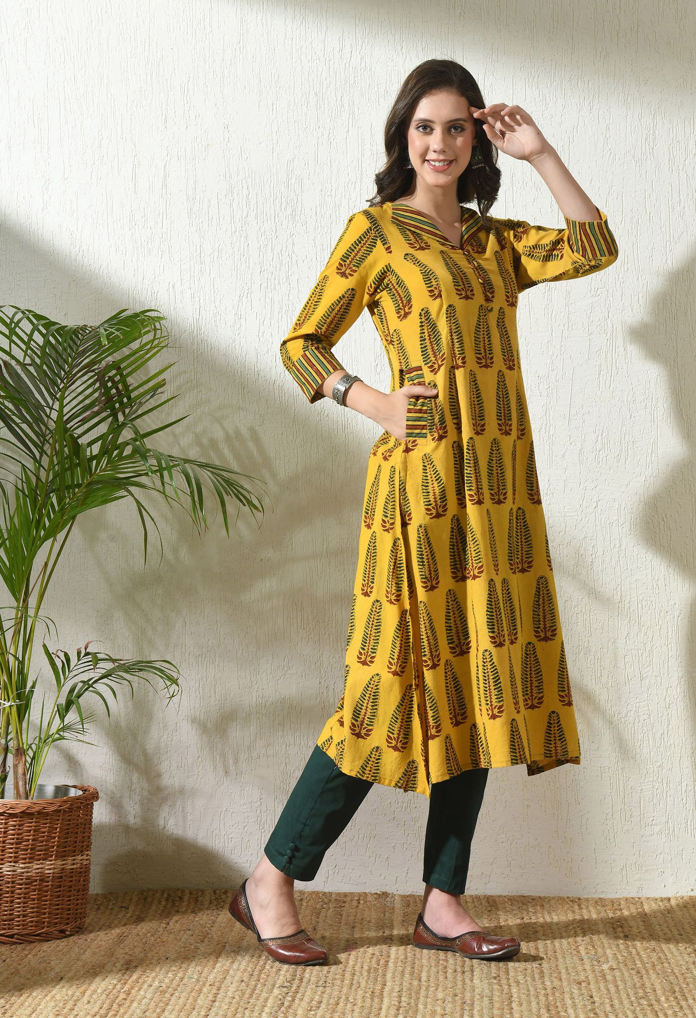 Woman wearing a yellow printed cotton kurta, dark cropped trousers and flat shoes.
