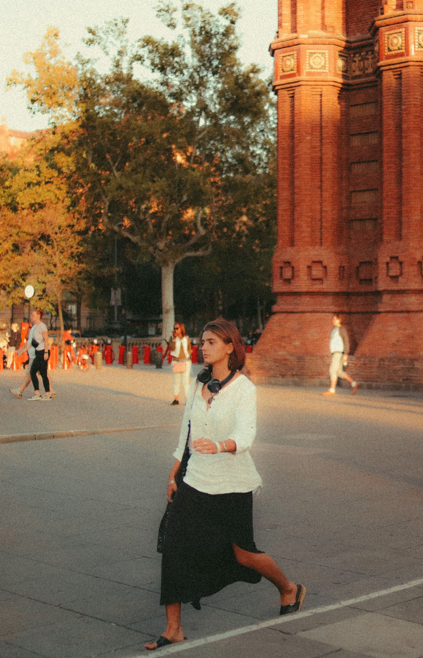 Woman walking in a white blouse, dark midi skirt and flat shoes.