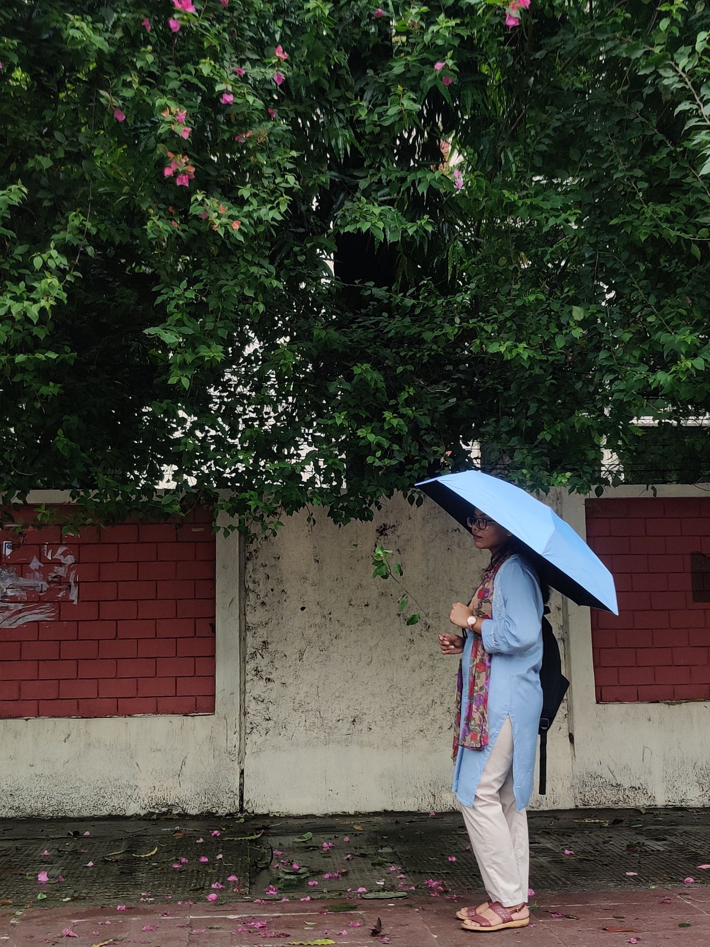 Woman carrying a blue umbrella above a pale kurta and cropped trousers.