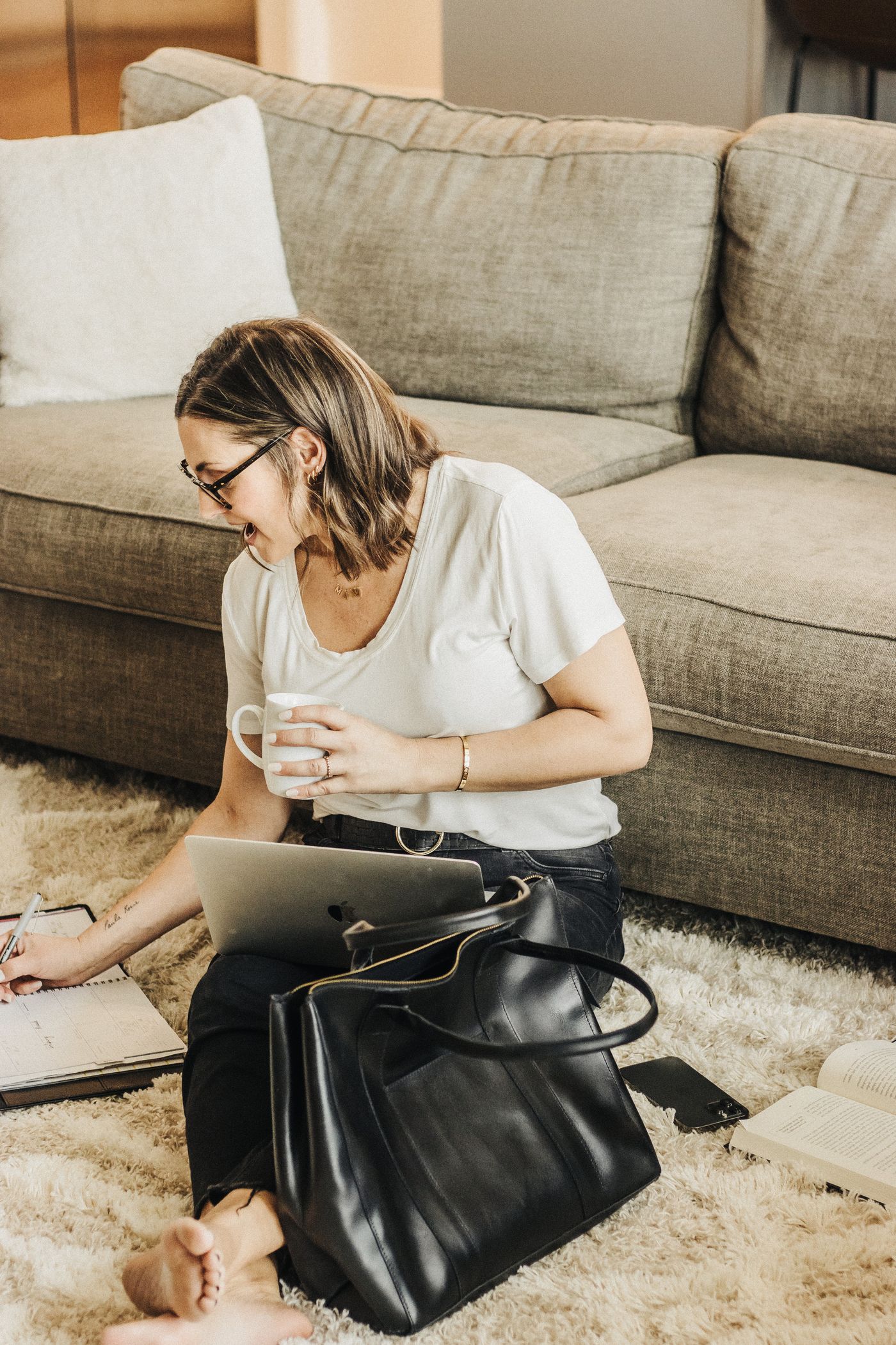 Woman with a black work tote beside her while using a laptop.