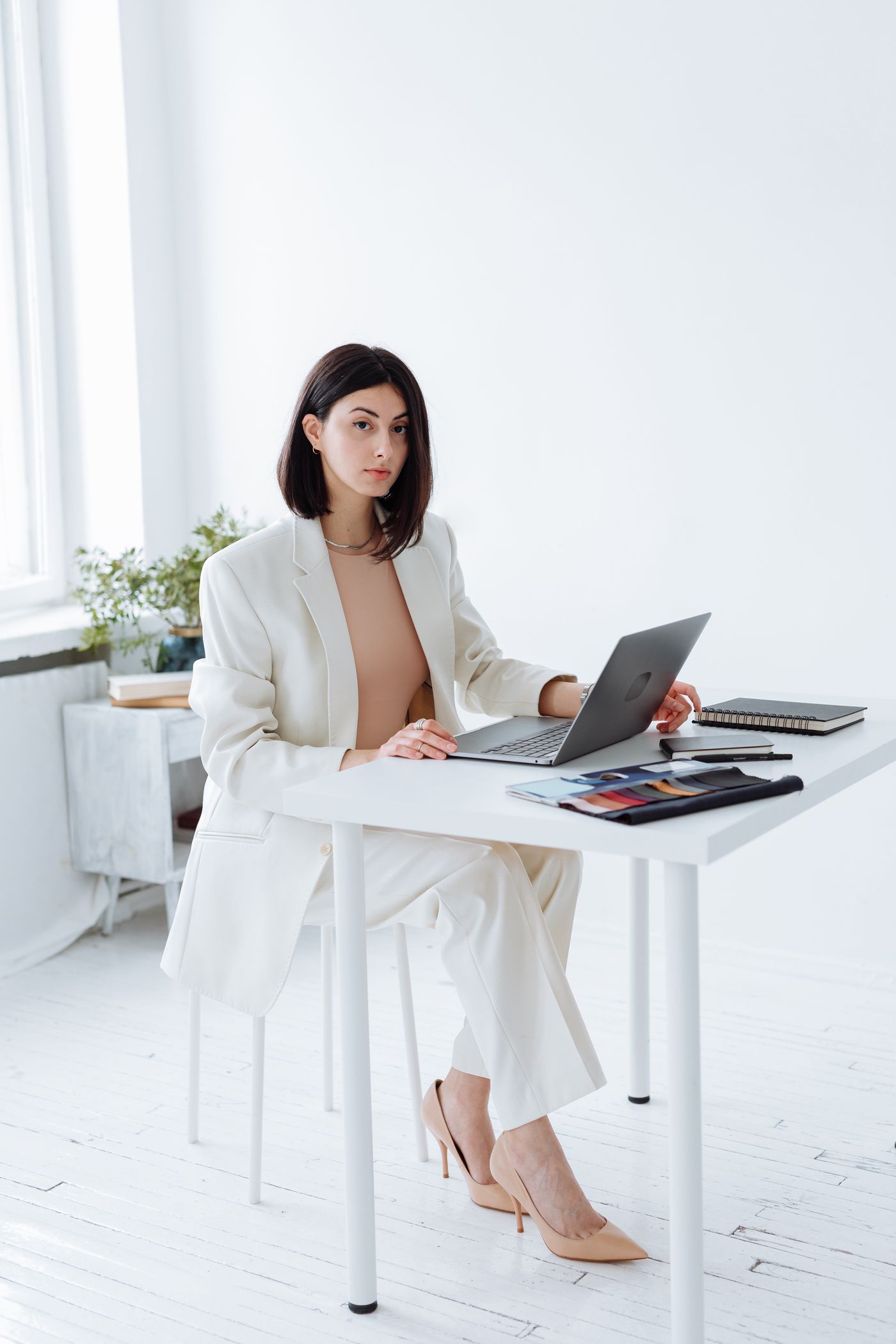 Woman in a white trouser suit using a laptop at a shared table.