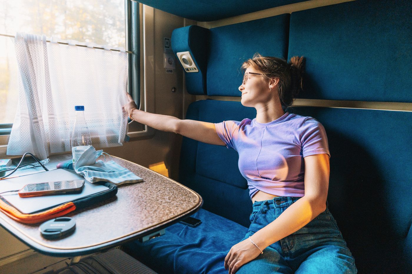 Woman seated in a train cabin wearing a T-shirt and blue jeans.