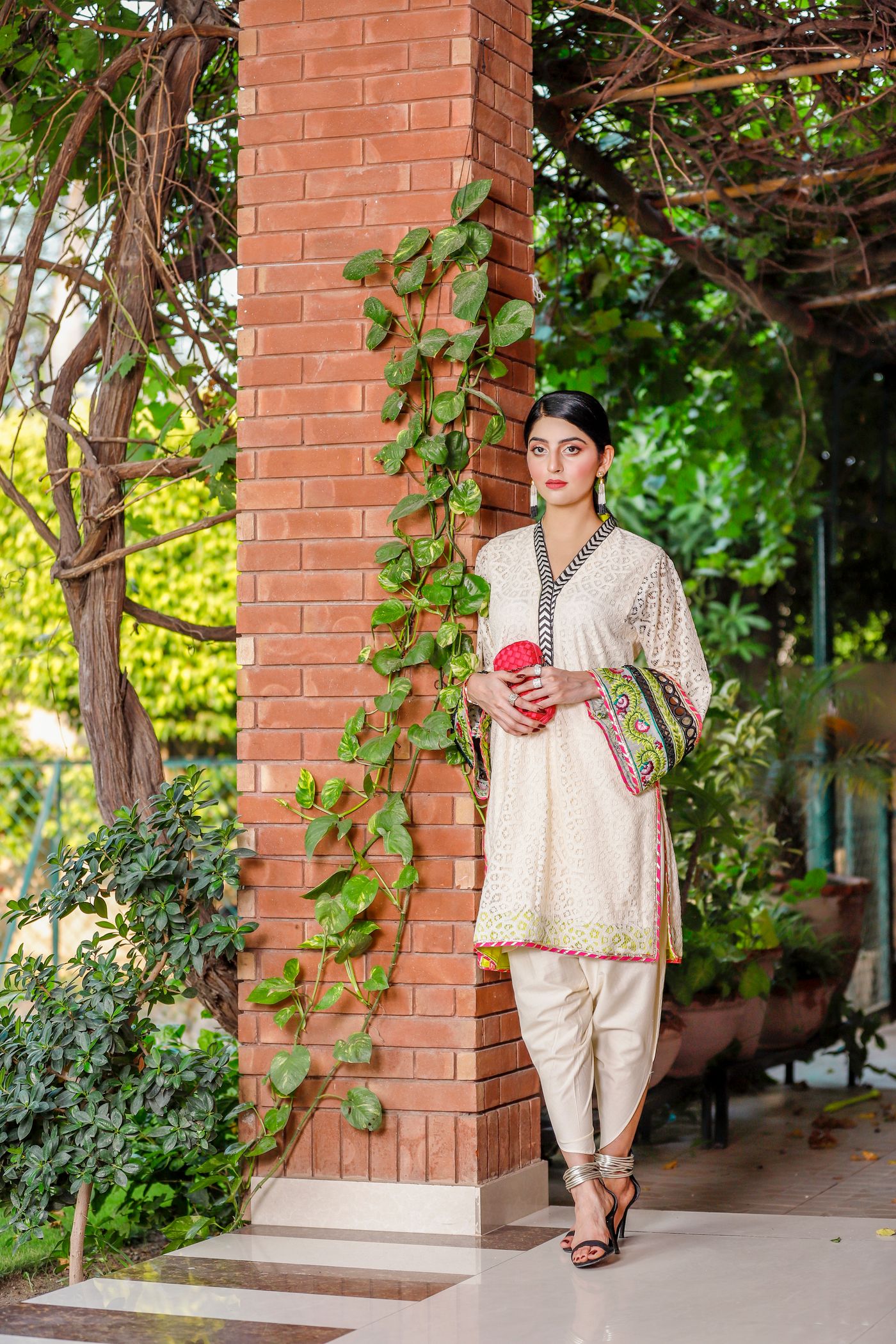 Woman wearing a pale straight kurta and narrow trousers beside a brick column.