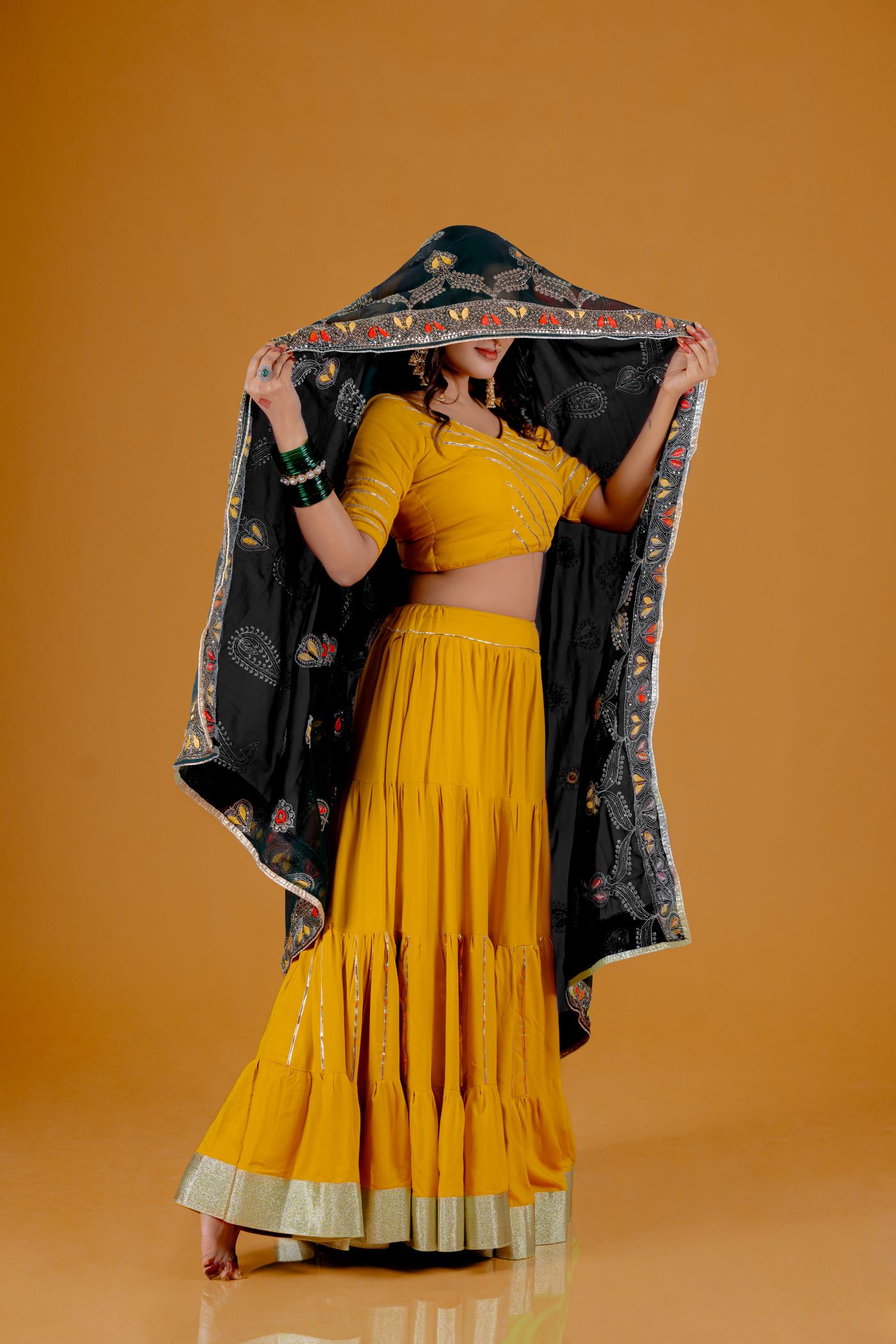Woman wearing a yellow plain blouse and long skirt with a dark patterned dupatta.