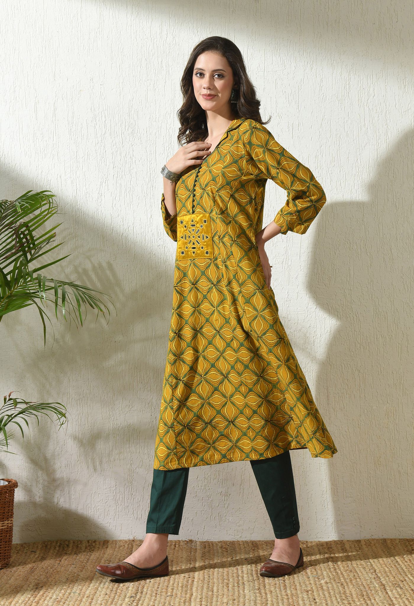 Woman wearing a yellow geometric printed kurta with dark trousers and flat shoes.
