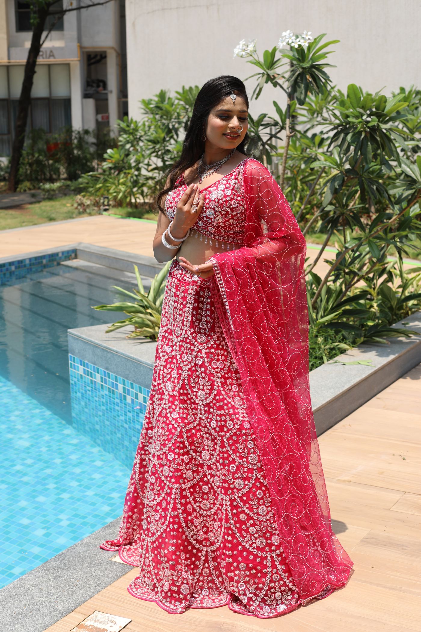 Woman wearing a red and white lehenga beside a pool.