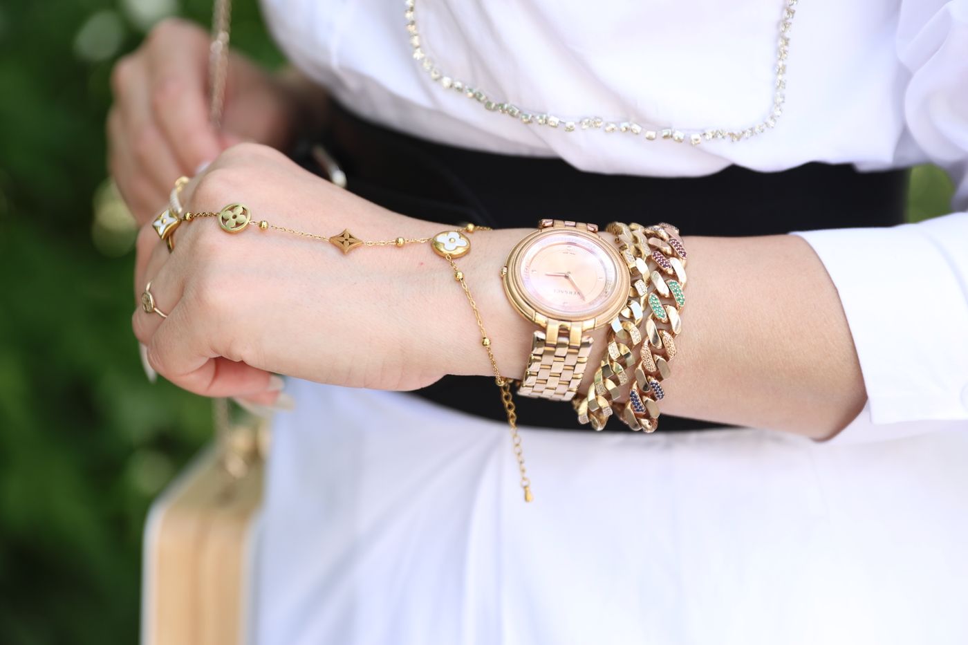 Gold-tone watch worn beside several bracelets on a woman's wrist.