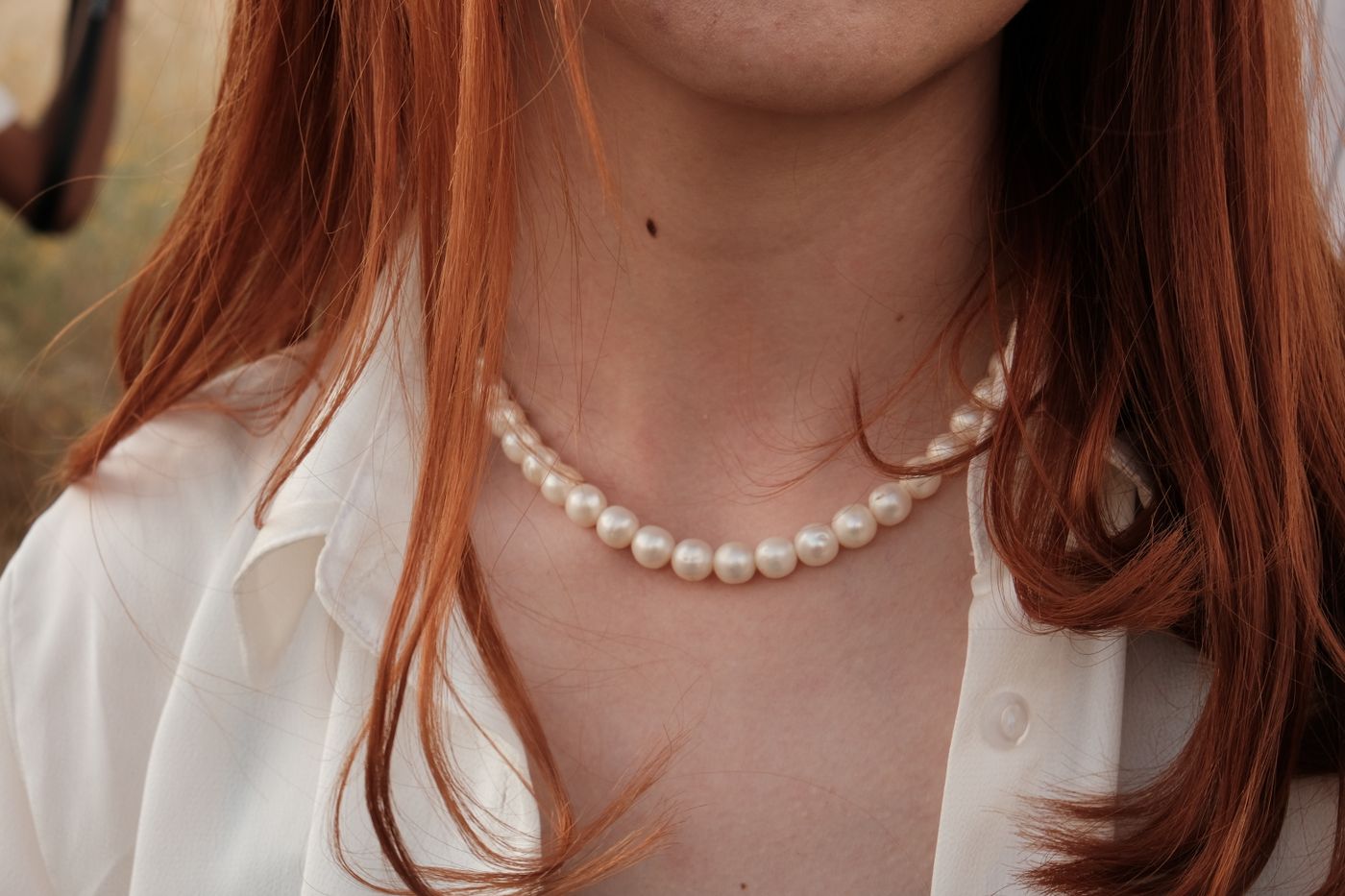 Pearl necklace worn at the open collar of a white shirt.
