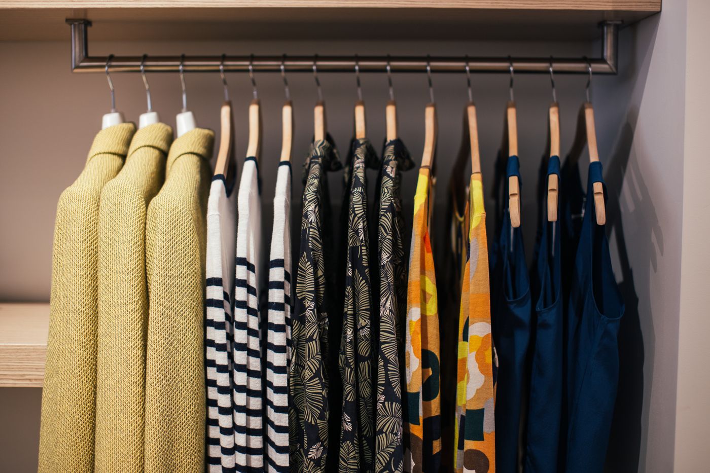 Clothes grouped along a wardrobe rail on wooden hangers.
